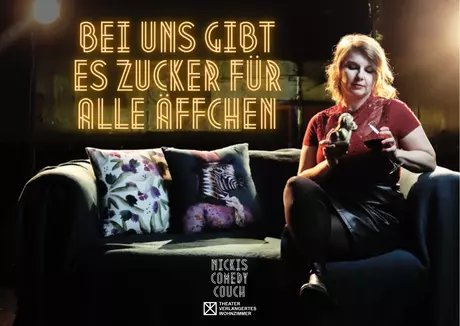Postkartenmotiv zur Veranstaltung. Im oberen Bereich steht in goldleuchtenden Neonbuchstaben: "Bei uns gibt es Zucker für alle Äffchen". Darunter ein Sofa, auf dem die Gastgeberin Nicki mit einem Glas Rotwein in der Hand sitzt. In der anderen Hand hä