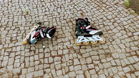 Zwei Inlineskater liegen auf Pflastersteinen