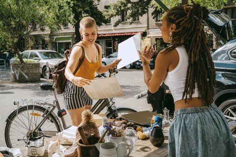 Female owner communicating with customer holding records while shopping at flea market