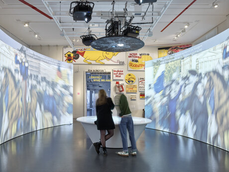 Besucher:innen der Ausstellung BERLIN GLOBAL beim Rad der Geschichte, einem Display-Tisch, im Raum Revolution