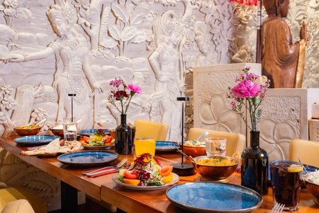 Amrit Restaurant – Gedeckte Tafel vor Steinrelief mit Buddha-Statue