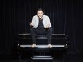 Florian Wagner sitzt auf einem Klavier auf einer schwarzen Bühne