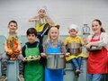 Gruppenfoto: 6 Kinder mit Töpfen, Gemüse und bunten Kochschürzen in der Küche des Kindermuseums unterm Dach
