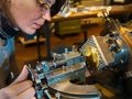 Eine Frau bedient eine Guillochier-Maschine. Mit der rechten Hand bewegt sie die Graviernadel der Maschine über das eingespannte Metallstück.