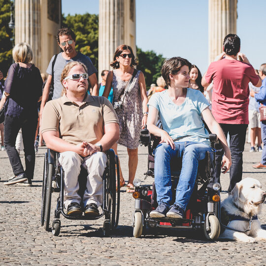 Two visitors in a wheel chair in front of the Brandenburger Tor