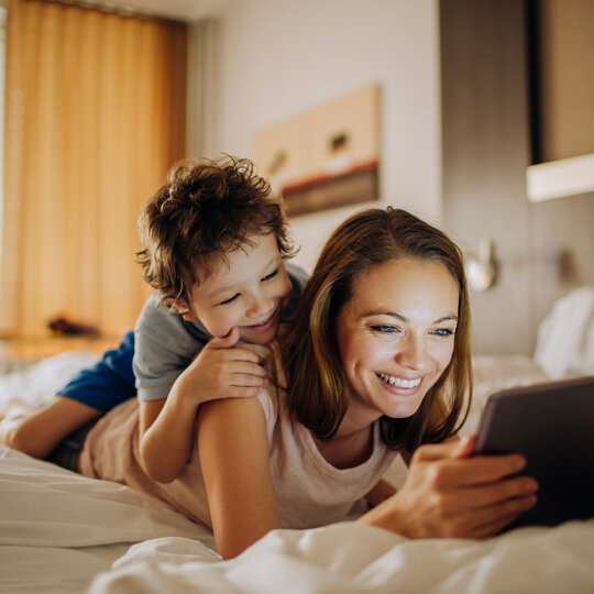 Mother and child lying on a bed and look at pictures on a tablet