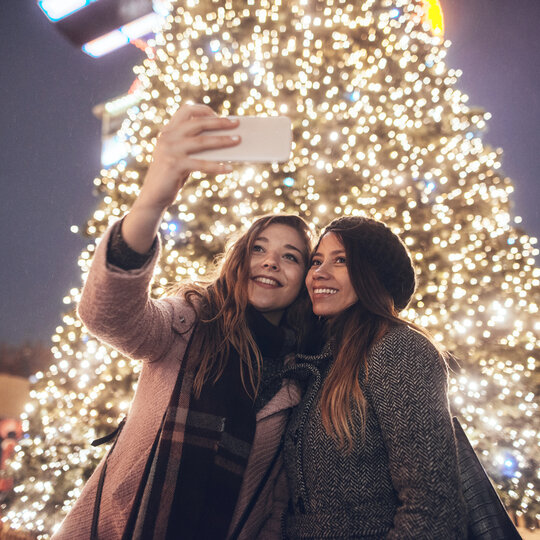 Girlfriends doing selfie in front of christmas tree.
