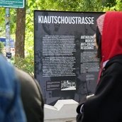 Die „Kiautschoustraße“ wurde 1905 nach der deutschen Kolonie Jiāozhōu an der chinesischen Ostküste benannt. Die Gedenkstele erklärt den kolonialen Kontext des Straßennamens und ergänzt ihn um antikoloniale Gegenerzählungen.