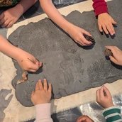 Experimentieren mit Ton: Kinderhände machen Muster in eine Tonschicht