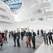 Das Ensemble steht in einem hellen, modernen Atrium. Die Decke ist aus Glas und mehrere Stockwerke sind erkennbar.