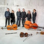 Das Ensemble steht an einer Wand. Ihre Instrumente liegen vor ihnen auf dem Boden.