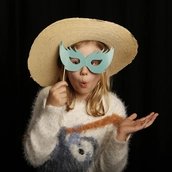 Theaterworkshop: Ein Mädchen mit Strohhut hält sich eine Augenmaske am Stab vor das Gesicht