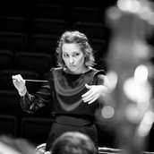 Dirigentin Ustina Dubitsky  steht vor dem Orchester und gibt mit dem Taktstock in der linken Hand den Einsatz.