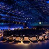 In einer großen Halle formen zahlreiche Klaviere eine Ellipse um das Publikum herum.