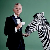 Max Raabe mit einer Tasse in der einen Hand und einer Untertasse in der anderen Hand, von der ein Zebra spielt