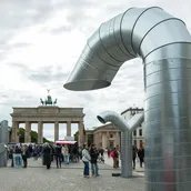Zwei große, gebogene Metallstrukturen stehen auf dem Pariser Platz vor dem Brandenburger Tor. Menschen versammeln sich in der Nähe.