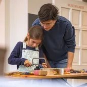 Mann und Kind beim gemeinsamen Sägen für ein Musikinstrument im Museumslabor