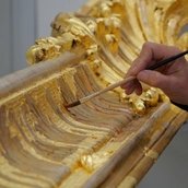 Rahmenrestaurierung, eine Hand führt einen Pinsel, mit dem Blattgold auf einem Bilderrahmen glattgestrichen wird