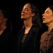 Drei Personen singen mit geschlossenen Augen. Die Lichtstimmung ist düster.