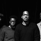 Vier Musiker stehen nebeneinander und schauen ernst