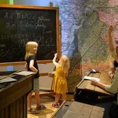In der Ausstellung BerlinZEIT spüren Eltern mit Kindern umgeben von historischem Mobiliar den Schulalltag der Kaiserzeit nach.