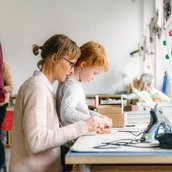 Eine erwachsene Person und ein Kind sitzen an einem Werktisch im Atelier Bunter Jakob und toben sich kreativ aus.