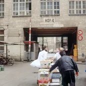 Drei Männer schieben eine mit Kisten beladene Karre durch einen Hinterhof