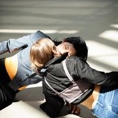 Zwei Personen liegen einander versetzt gegenüber auf dem Boden in der Sonne. Ihre Münder berühren sich.