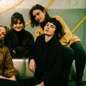 Vier junge Musiker:innen sitzen auf einer Bank und stecken die Köpfe zusammen Vier junge Musiker:innen sitzen auf einer Bank und stecken die Köpfe zusammen