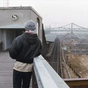 Mann auf Brücke mit S-Bahn-Eingang blickt über eine Baustelle auf eine Brücke