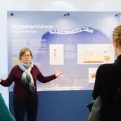 Vermittlerin vor Ausstellungswand Körperschleime