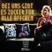 Postkartenmotiv zur Veranstaltung. Im oberen Bereich steht in goldleuchtenden Neonbuchstaben: "Bei uns gibt es Zucker für alle Äffchen". Darunter ein Sofa, auf dem die Gastgeberin Nicki mit einem Glas Rotwein in der Hand sitzt. In der anderen Hand hä
