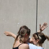 Zwei junge Frauen stehen dicht beieinander und verschränken ihre Arme ineinander.