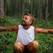 Xavier Rudd in einem Wald hockend