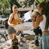 Female owner communicating with customer holding records while shopping at flea market