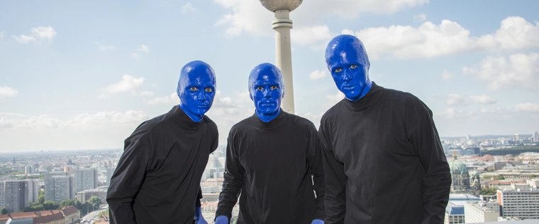 Die BLUE MAN GROUP posiert vor dem Fernsehturm bei strahlend blauem Himmel.