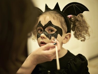 Mother painting daughters face for halloween bat costume