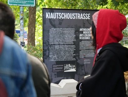 Die „Kiautschoustraße“ wurde 1905 nach der deutschen Kolonie Jiāozhōu an der chinesischen Ostküste benannt. Die Gedenkstele erklärt den kolonialen Kontext des Straßennamens und ergänzt ihn um antikoloniale Gegenerzählungen.