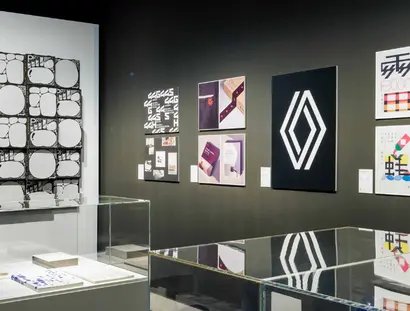 Blick auf an Wänden gehängte Plakate und Vitrinen mit Objekten im Vordergrund