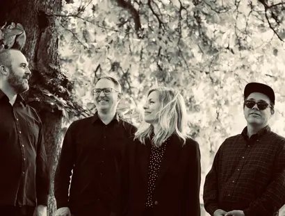 Die Band steht unter einem Baum, die Gesichter fröhlich