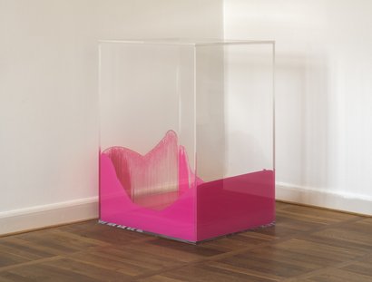 Ein Kubus aus Acrylglas mit pinker Farbe im Innern, die an den Seitenwänden Spuren der Bewegung hinterlassen hat.