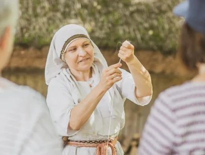 Eine Frau in Gewandung mit einem gespannten Wollfaden in der Hand während einer Vorführung im Museumsdorf Düppel