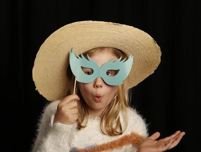 Theaterworkshop: Ein Mädchen mit Strohhut hält sich eine Augenmaske am Stab vor das Gesicht