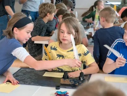 Kinder im Museumslabor schreiben mit Tinte und Feder