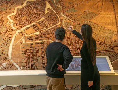 Besucherin und Besucher vor einem Stadtmodell mit Medienstation