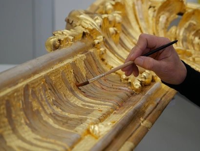 Rahmenrestaurierung, eine Hand führt einen Pinsel, mit dem Blattgold auf einem Bilderrahmen glattgestrichen wird