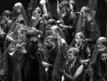 Musiker:innen spielen ihre Instrumente. Durchsichtige Tücher liegen über ihren Köpfen.