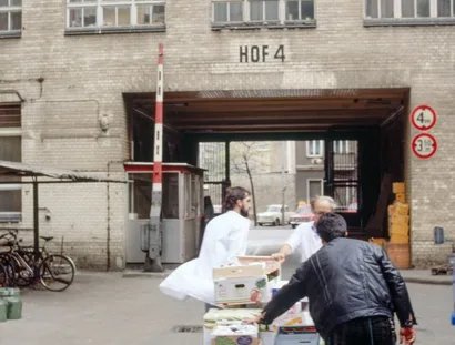 Drei Männer schieben eine mit Kisten beladene Karre durch einen Hinterhof