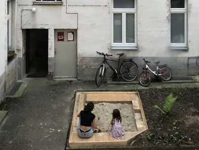 Frau mit Kind im Sandkasten eines Berliner Hinterhofs