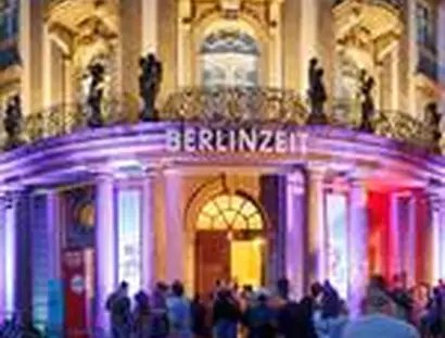 Das Museum bei Nacht von außen mit bunter Leuchtschrift, auf der BERLINZEIT steht, davor Menschen